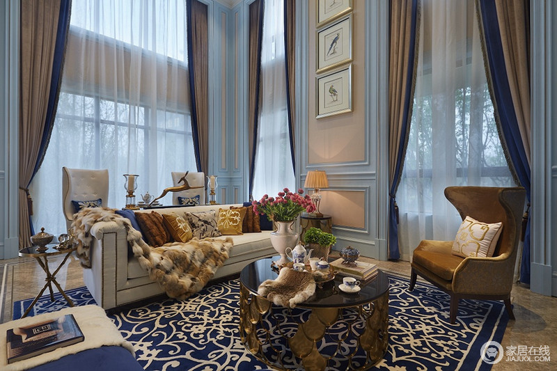 客厅有着丰富的玻璃窗，带来极佳视觉和采光，令空间十足通透；浅蓝色的墙面上石膏线的刻画立体又显质感，搭配着柔和的窗纱帘，烘托着空间的优雅气质；沙发组粗犷中有着细腻，蓝底印花地毯华美动人，赋予空间的格调典贵多姿。