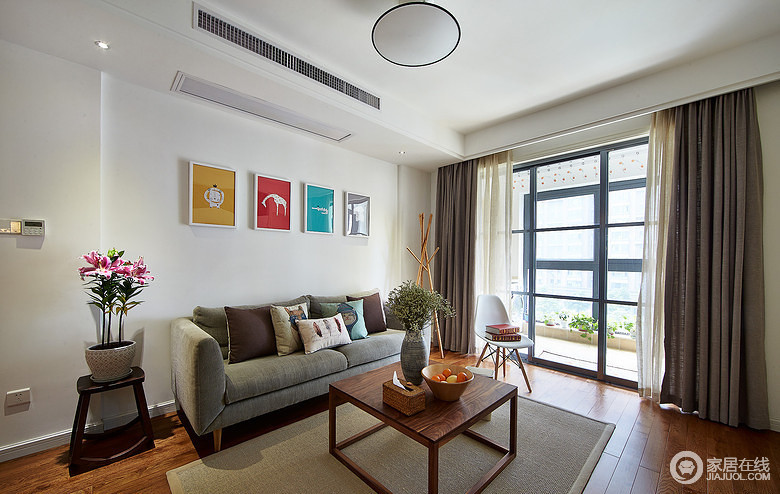 客厅采用的非常简约的现代风格，白色的墙面上悬挂了画框，带有一种文艺气息；灰绿色的布艺沙发柔软舒和，搭配着原木地板，让空间显得清新又自然。

