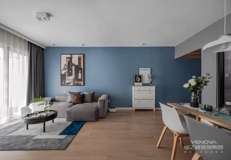 蓝色的沙发墙贯穿到玄关，挂上一大幅画，结合灰色布艺沙发，地面还垫着简约灰色的地毯，沙发侧边还有个小斗柜，整体空间设计显得安静优雅好舒适。