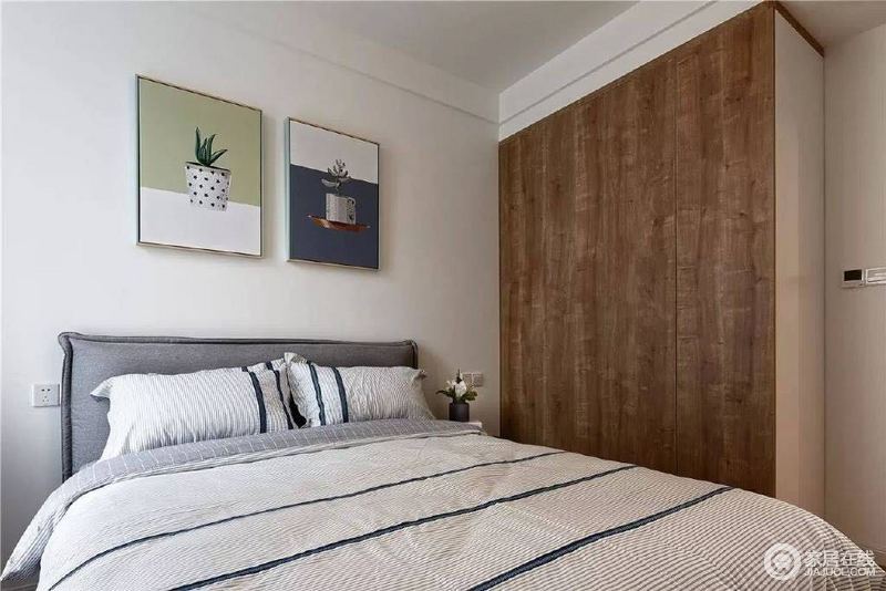 卧室将实木衣柜与墙体连为一体，增加了生活的储存空间，胡桃色实木的质感更是凸显品质；两幅清新的画作缓解了灰色床品的朴素，颇显舒适。