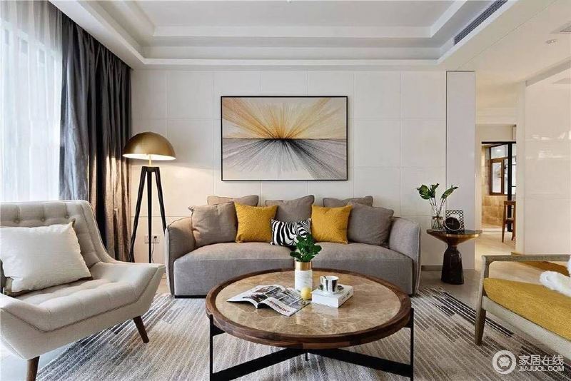 客厅中的沙发背景墙以一副抽象挂画蔓延出光线，灰色布艺沙发的柔软与地毯的条纹朴素之中，多了简约艺术；落地灯与各式圆几柔化了空间，呈现出方圆之美。