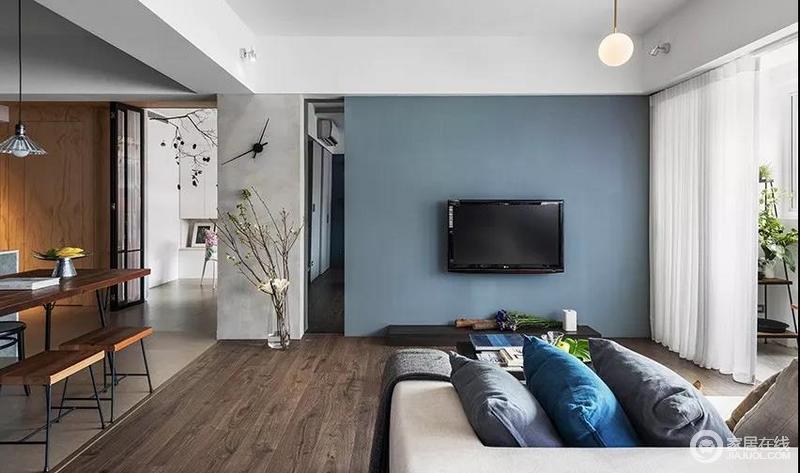 客厅刷了一面灰蓝色电视背景墙，有一种优雅稳重的气息；水泥梁柱和电视墙间设计了镜面，延伸视觉范围，让空间显得更有层次。
