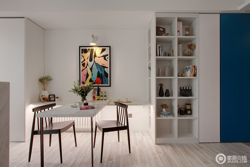  空间涂刷为白色，清晰而白净的基调，与浅木纹地面构成温和的局面；柜体串联转折，连接至厨房，并延伸出二人餐桌构同一体，更为整洁；简洁个性的实木椅子与彩色艺术画调染出现代时髦感。