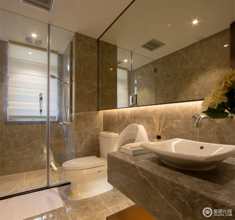 简约的卫生间以细腻肌理的灰黄大理石铺陈，营造出内敛朴实的格调。浴室镜下方内置灯带装饰，营造出精致质感。清玻璃材质通透，有效分隔出干湿区域，并利于空间沟通。