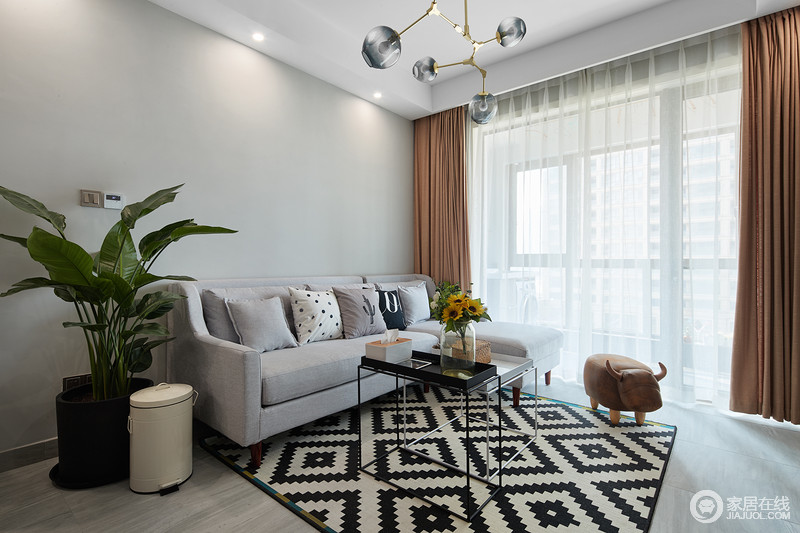 客厅的浅灰色沙发采用布艺代替，与黑白纹路的地毯相映，本来是中规中矩的黑白灰三色的搭配，在此基础之上搭配橘色元素的软饰，让空间一下子活泼起来。大胆的色彩搭配，总能在稳重中搭出新意，让