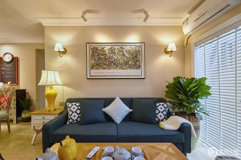 沙发两侧分别摆放着一盆琴叶榕和黄色的台灯，安静而美好