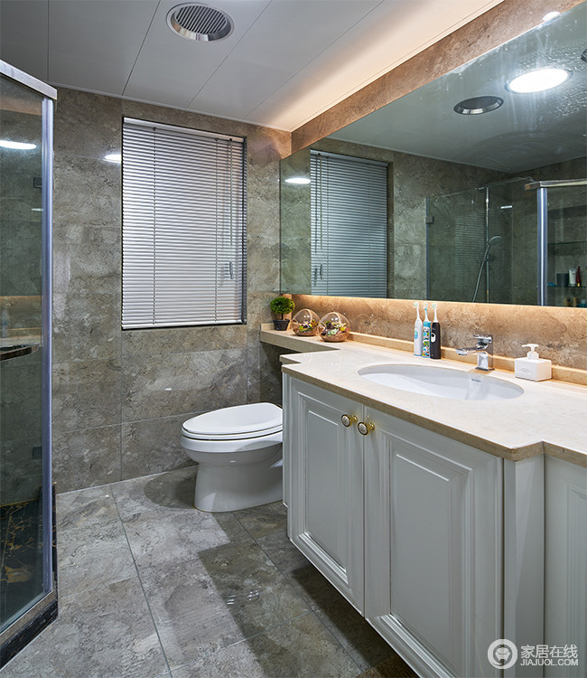 卫浴间采用浅灰色大理石纹的防滑砖，色彩搭配低调朴素。耐脏防滑的瓷砖非常实用。镜子周围一圈橘黄的灯光是点缀空间的亮点，弱化冷感增添空间的温馨感。