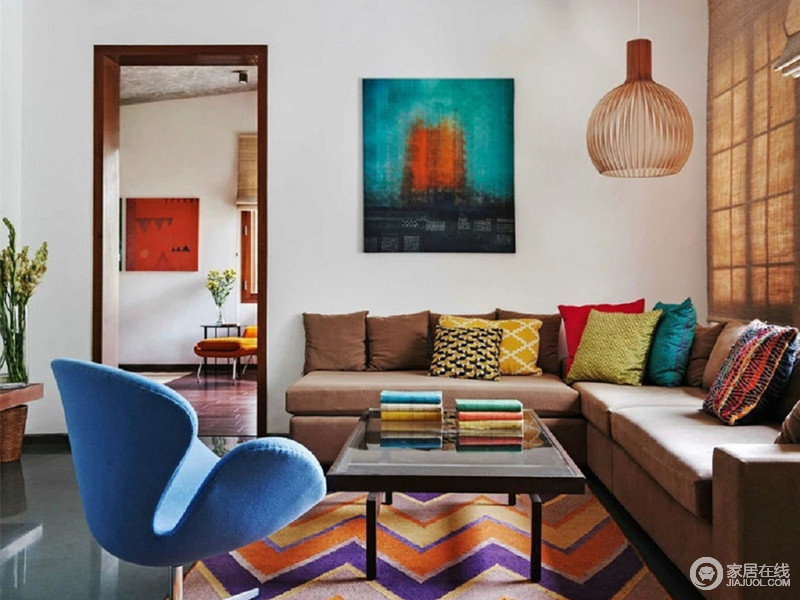 白墙灰地，褐色L型布艺沙发在彩色靠垫的装点下散发着波西米亚风；在最美的时空里，因为紫色和黄色波浪形地毯和蓝色椅子而变得明快亮丽。
