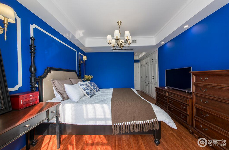 卧室里宝蓝色纯粹又鲜亮，带着珠光的深邃优雅，大面积运用在墙面上，渲染出的休憩氛围宁静温柔；木色的家具和地面与墙面形成反差的对比，在阳光的映照下，层次丰富的空间休闲逸趣；拐角处，整体白色衣柜入墙，丰富了空间强收纳功能。