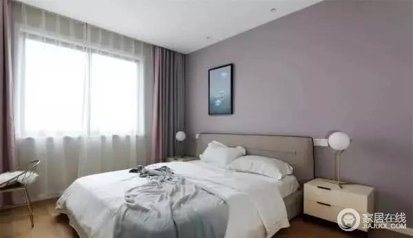 主卧室的背景墙刷成了更为优雅的灰紫色，墙面的挂画和床上的毯子相互呼应，左右两侧的台灯简洁而又精致，床尾还有设计了一个梳妆台。