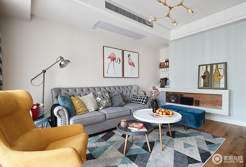 客厅色彩的搭配以灰色为主，用亮丽的黄色和蓝色墙配饰作为跳色，让客厅的空间婉约高雅，火烈鸟的挂画带来生命的跃动，而拼色地毯，无疑，给空间更多的几何之美。