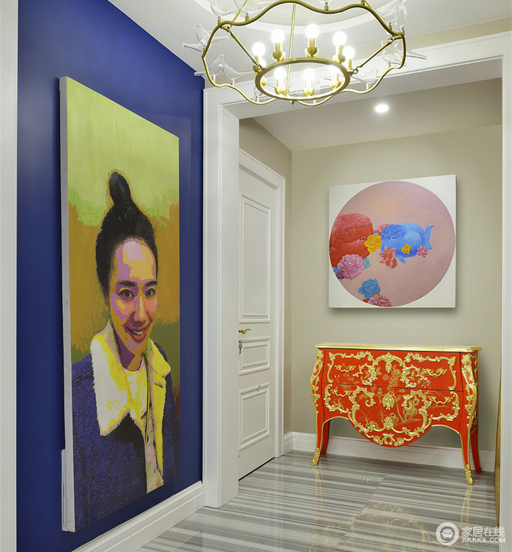 入户门厅里大面积蓝色墙面上主人巨幅肖像画，极具视觉冲击力；与驼色墙面上的花卉画作、中式描金雕花朱红柜，大胆演绎现代与复古的摩登搭配，空间一览趣味艺术。