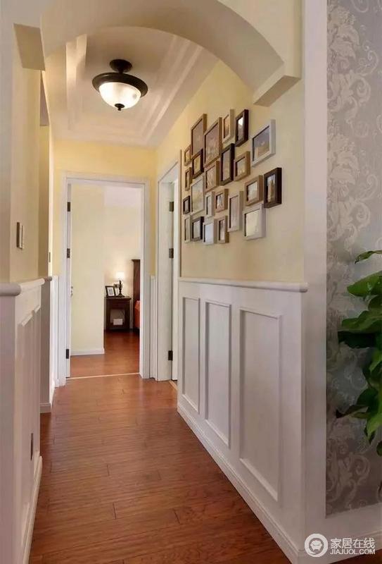 通往卧室的走道中间装了个拱门造型，墙脚也装了护墙板，右侧墙面上挂有一组温馨的照片。