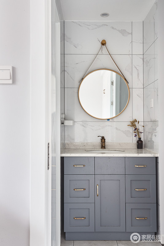 卫生间简单大气的白色瓷砖，搭配圆形金属边的镜子避免了空间的生硬和呆板；灰蓝色盥洗柜与白色台面构成和谐，让生活更为舒适。