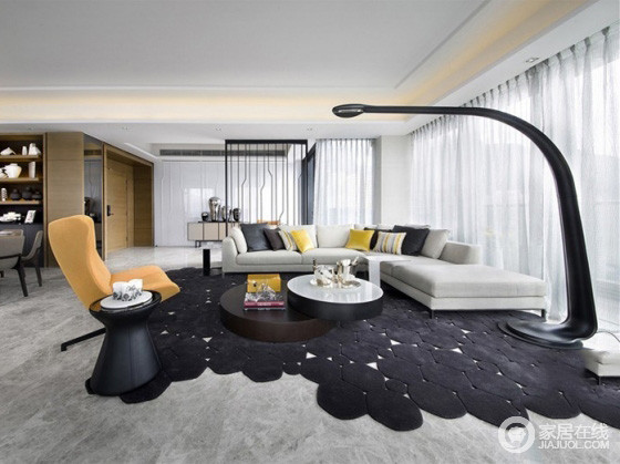 宽敞舒服的客厅。浅灰色曲形沙发放置在客 厅中央，搭配黑色座地灯﹑不规则图案黑色地毯