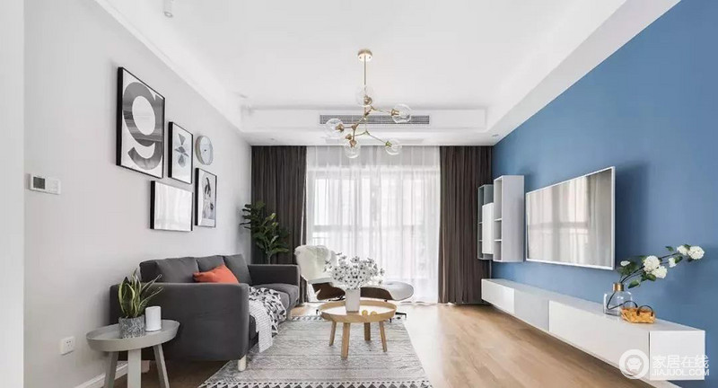 客厅地面通铺木色地板，墙面采用蓝灰两种色调，视觉上具有层次感。
