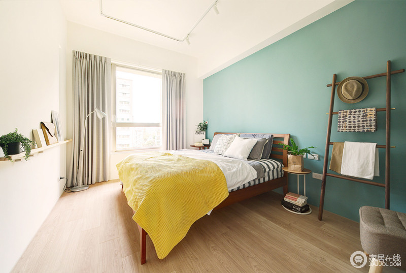 卧室以蓝色漆搭配黄色毛毯，让空间清新活力，十分明媚；银灰色窗帘搭配简约风的落地灯，与实木衣架和家具让空间延续简约之雅，木架上的绿植和饰物，让空间多了线条美学，让空间利整，满载简单和舒适。