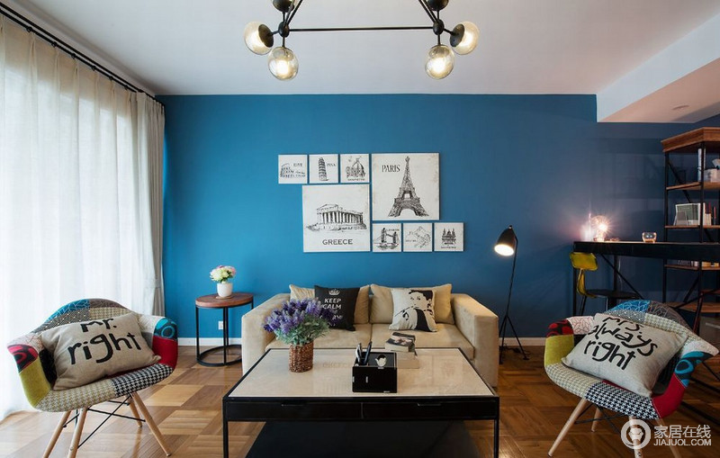 客厅里大面积的深蓝色墙面，带来宛如海洋般的深邃感，平和的木质地板则调和了空间氛围。装饰的画作、靠包及座椅上的拼接布艺，带来复古小资文艺情怀。